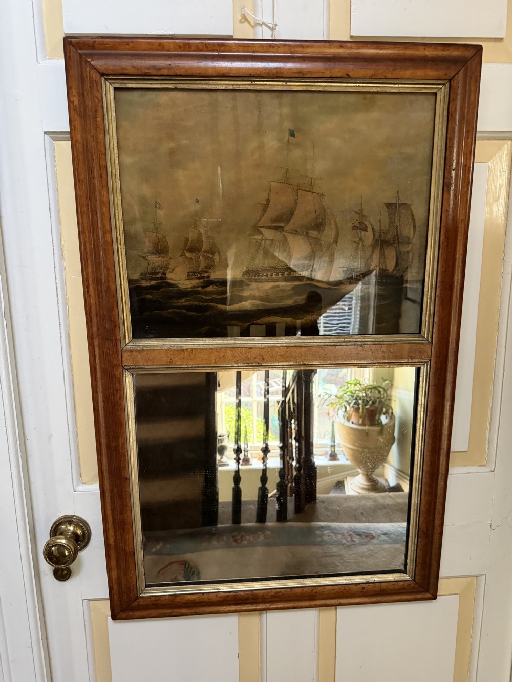 An early nineteenth-century rectangular maple-framed divided mirror featuring a reverse glass print of a naval engagement in the upper section and a reflective mirror below. View XV