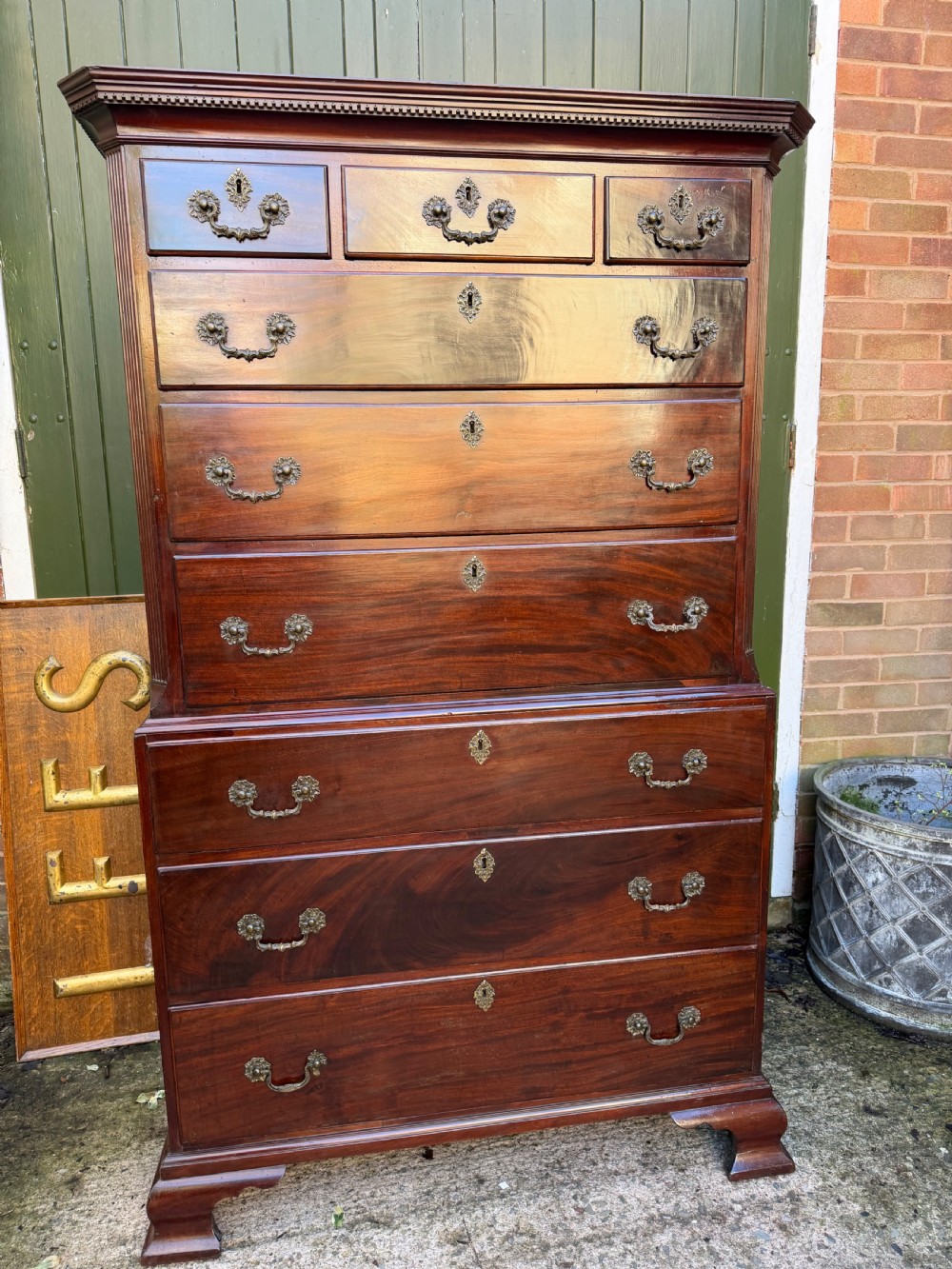 A mid-18th century George II red walnut chest-on-chest featuring a dentil moulded cornice, brass swan-neck handles, and bracket feet.