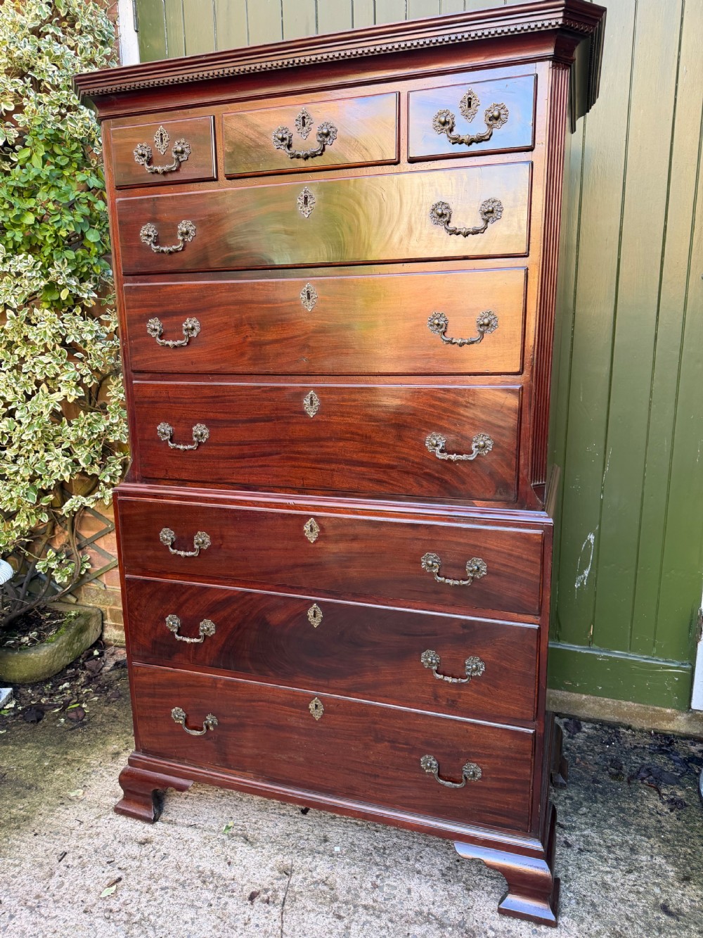 A mid-18th century George II red walnut chest-on-chest featuring a dentil moulded cornice, brass swan-neck handles, and bracket feet. View IV