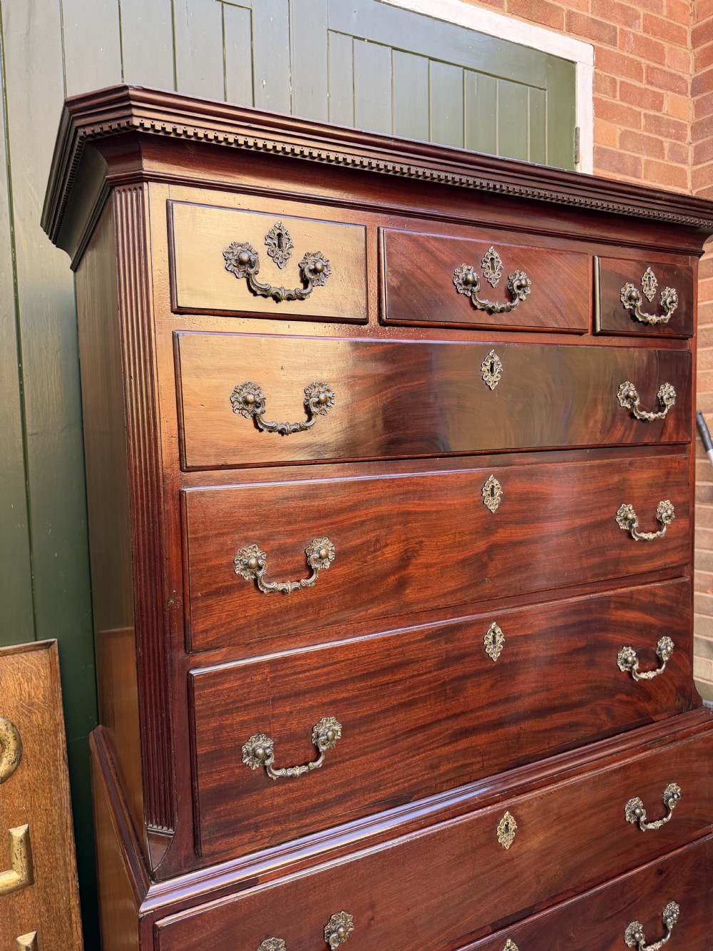 A mid-18th century George II red walnut chest-on-chest featuring a dentil moulded cornice, brass swan-neck handles, and bracket feet. View XXIII