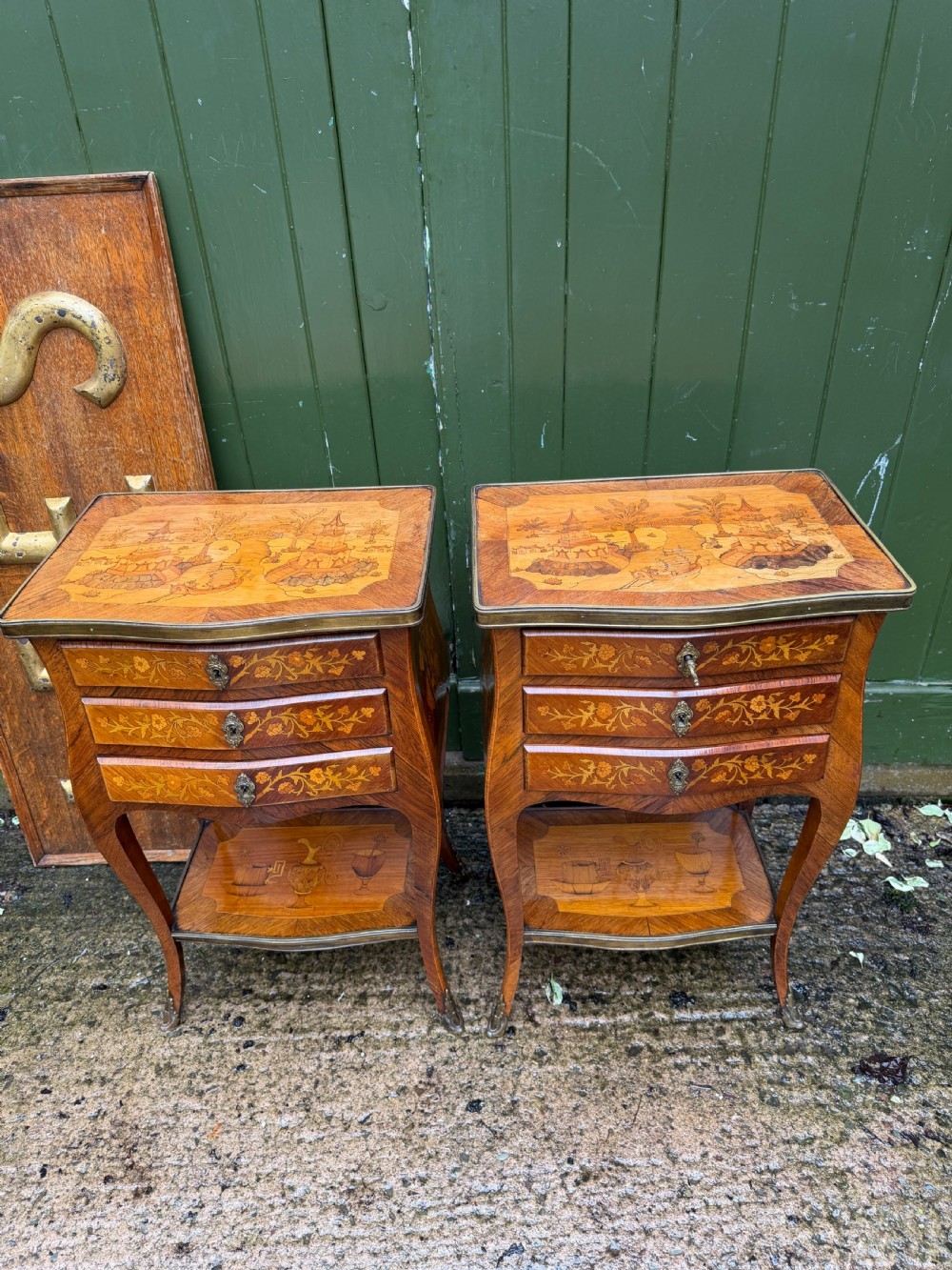 A pair of French marquetry bedside tables featuring three drawers with floral inlays, brass mounts, curved legs, and a lower tier shelf. View II