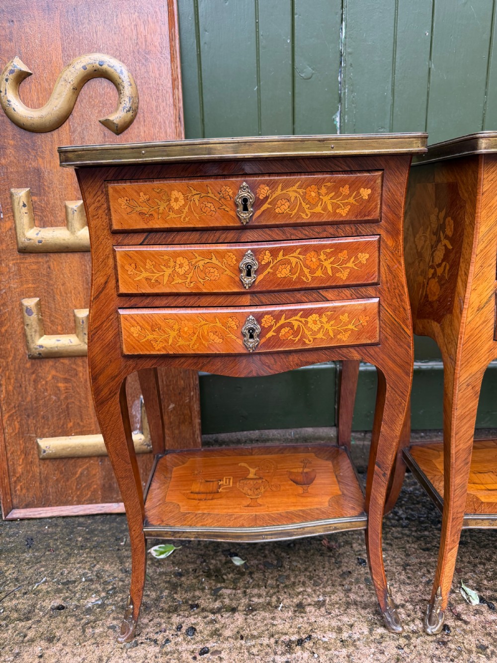 A pair of French marquetry bedside tables featuring three drawers with floral inlays, brass mounts, curved legs, and a lower tier shelf. View IV