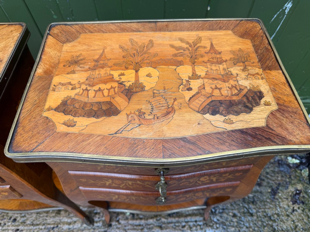 A pair of French marquetry bedside tables featuring three drawers with floral inlays, brass mounts, curved legs, and a lower tier shelf. View V