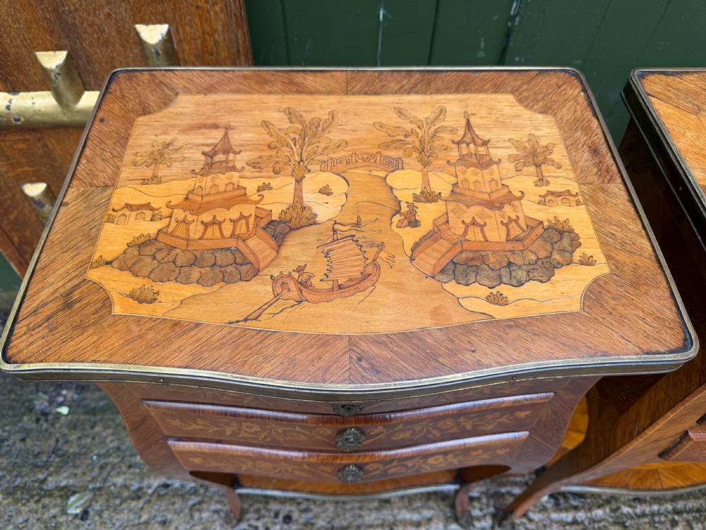 A pair of French marquetry bedside tables featuring three drawers with floral inlays, brass mounts, curved legs, and a lower tier shelf. View VI