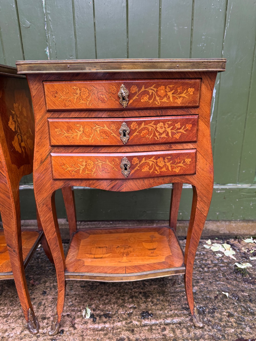 A pair of French marquetry bedside tables featuring three drawers with floral inlays, brass mounts, curved legs, and a lower tier shelf. View VII