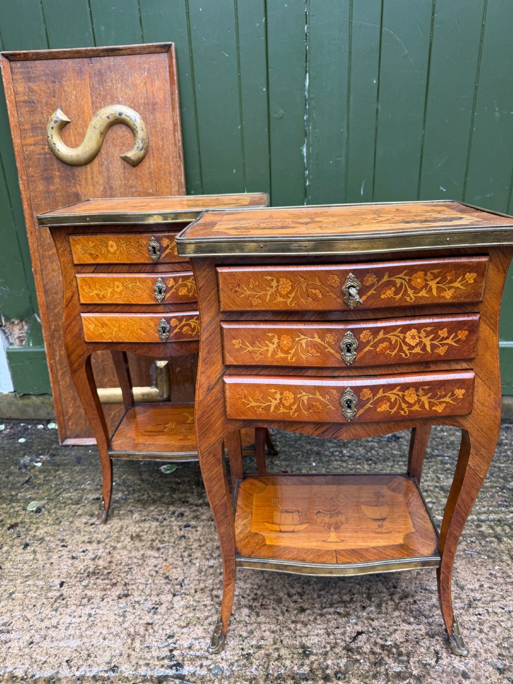 A pair of French marquetry bedside tables featuring three drawers with floral inlays, brass mounts, curved legs, and a lower tier shelf. View XV
