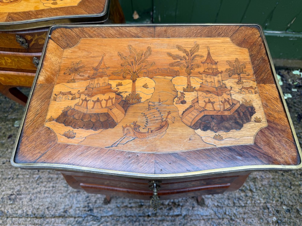 A pair of French marquetry bedside tables featuring three drawers with floral inlays, brass mounts, curved legs, and a lower tier shelf. View XVI