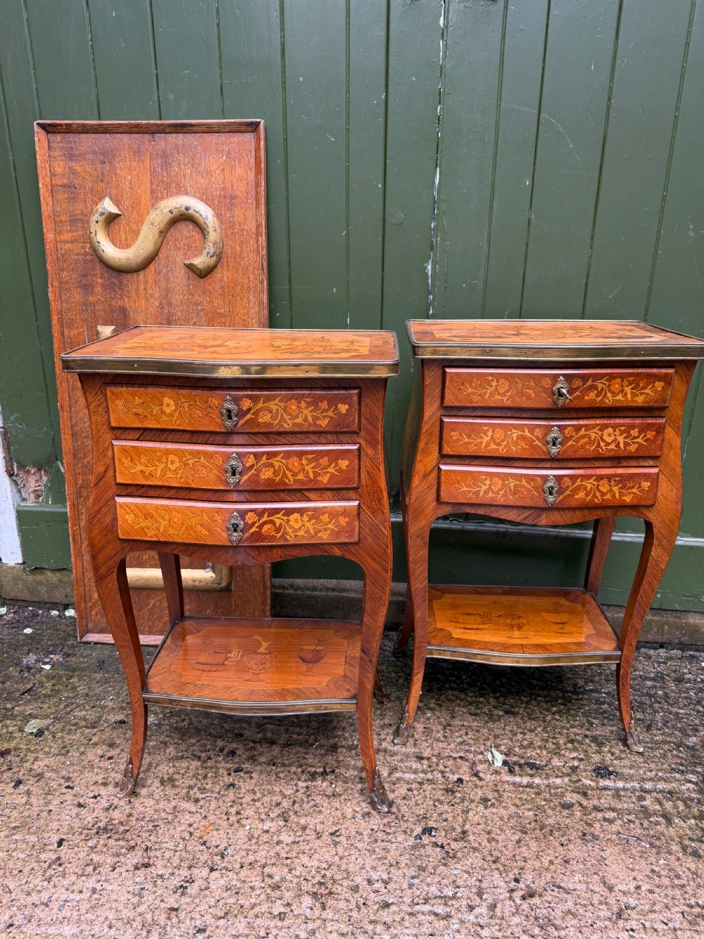 A pair of French marquetry bedside tables featuring three drawers with floral inlays, brass mounts, curved legs, and a lower tier shelf. View XXI