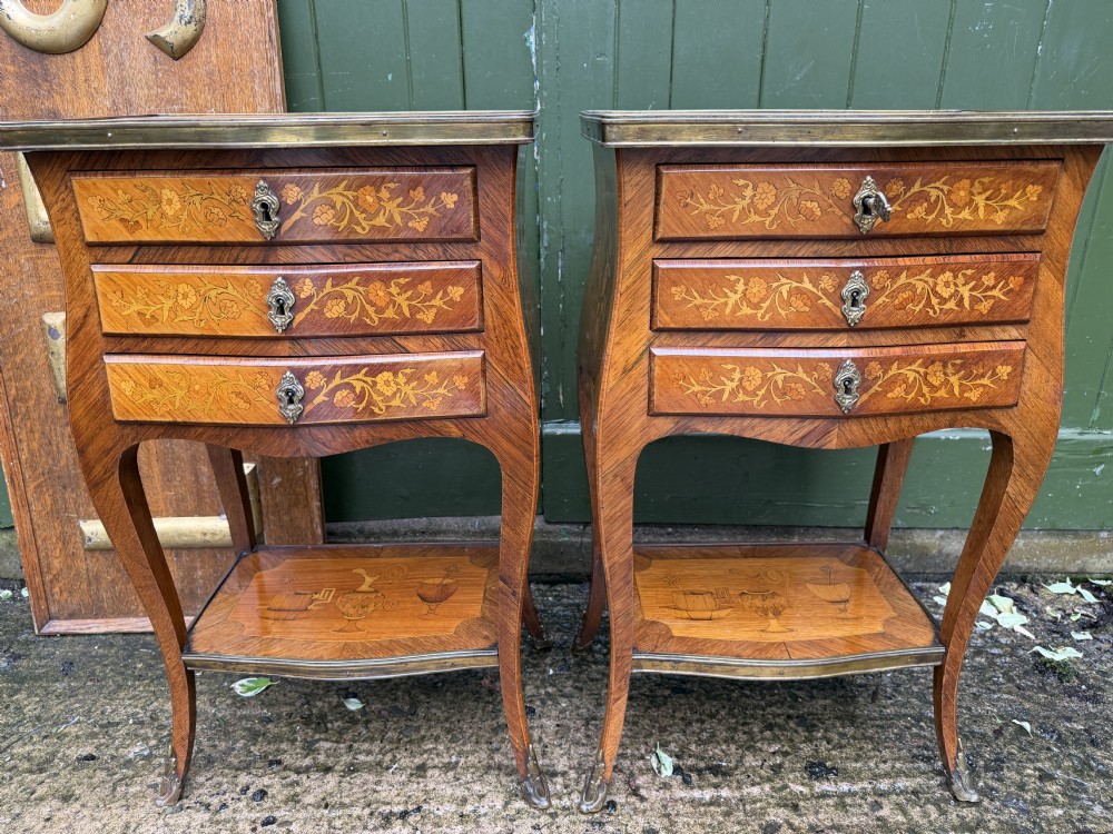 A pair of French marquetry bedside tables featuring three drawers with floral inlays, brass mounts, curved legs, and a lower tier shelf.