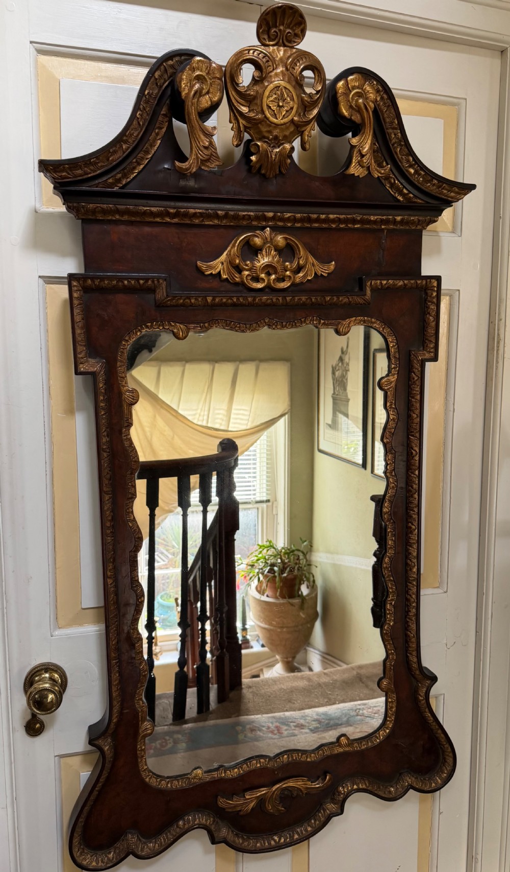 A George II style walnut wall mirror featuring a carved parcel gilt frame with a swan-neck pediment and central cartouche cresting.