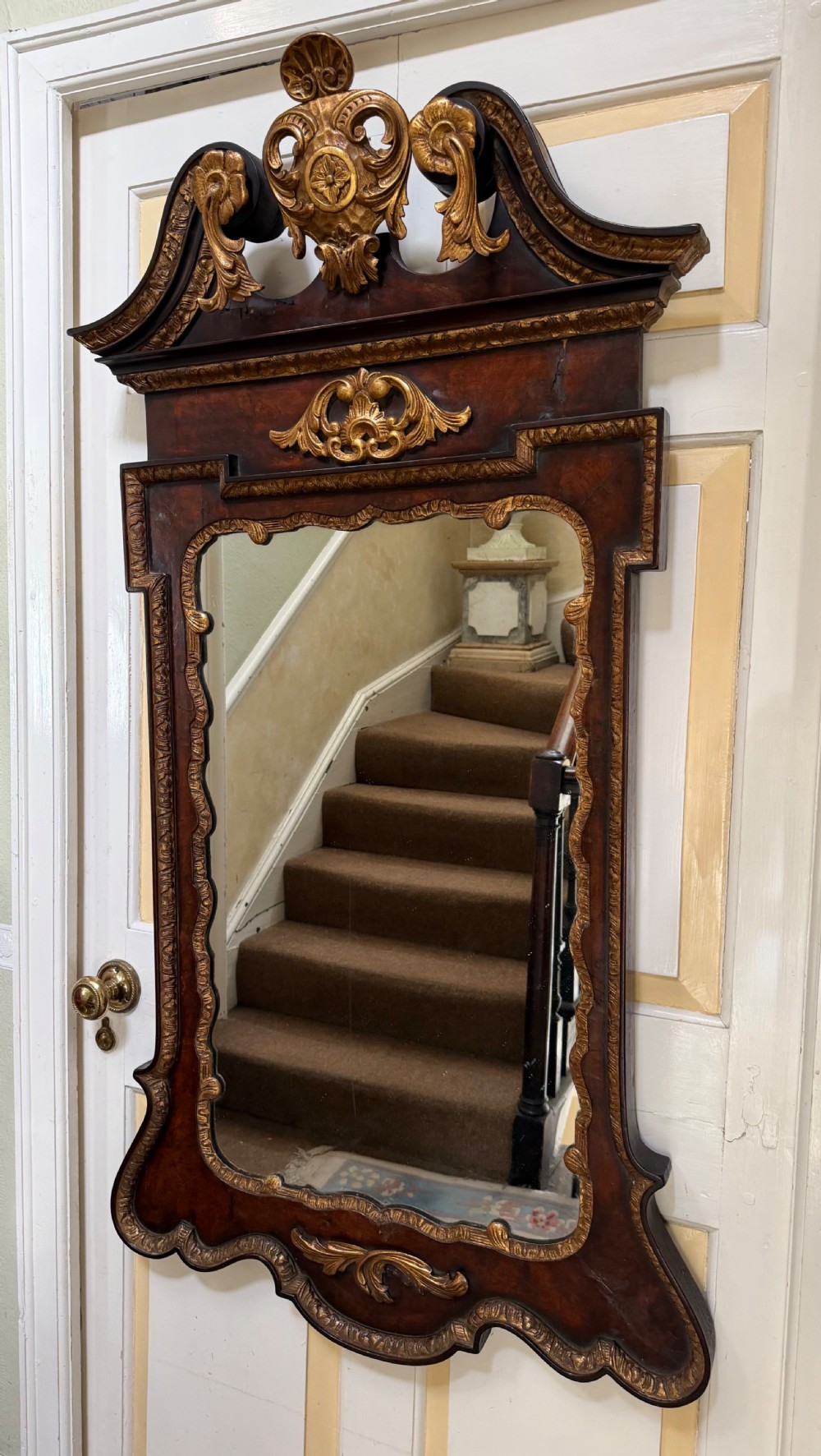 A George II style walnut wall mirror featuring a carved parcel gilt frame with a swan-neck pediment and central cartouche cresting. View II