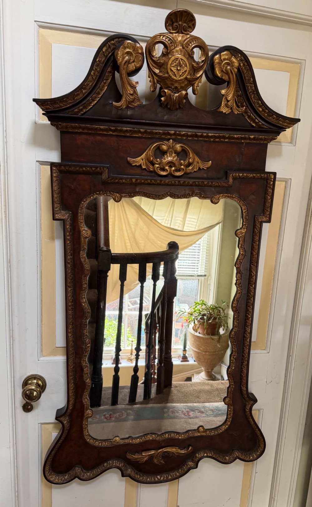 A George II style walnut wall mirror featuring a carved parcel gilt frame with a swan-neck pediment and central cartouche cresting. View III