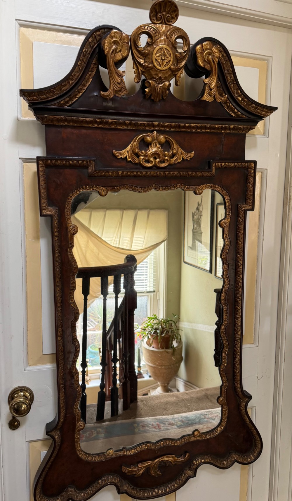 A George II style walnut wall mirror featuring a carved parcel gilt frame with a swan-neck pediment and central cartouche cresting. View V