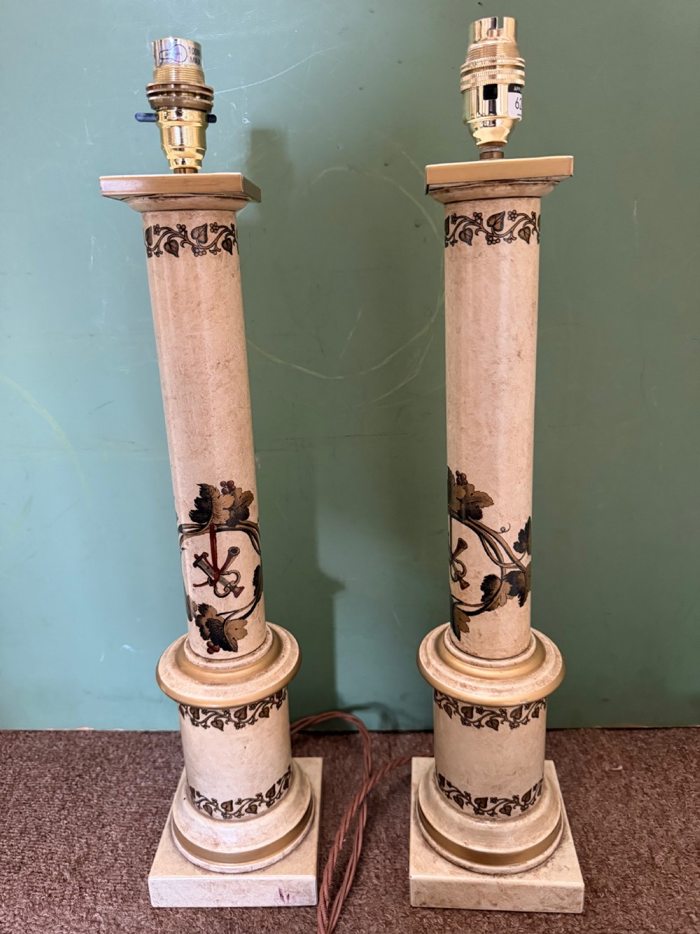 A pair of early twentieth-century French cream tole-peinte column table lamps decorated with hand-painted vine leaves, musical motifs, and gilt trim.