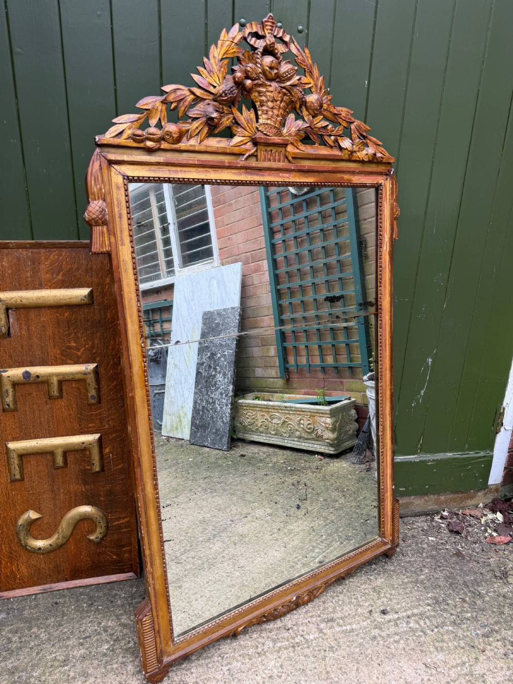 A large late eighteenth-century French giltwood wall mirror featuring a carved fruit basket pediment, floral foliage, and a rectangular beaded frame.