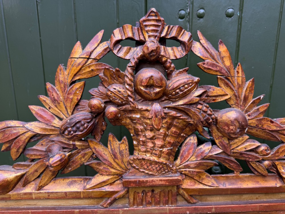 A large late eighteenth-century French giltwood wall mirror featuring a carved fruit basket pediment, floral foliage, and a rectangular beaded frame. View II