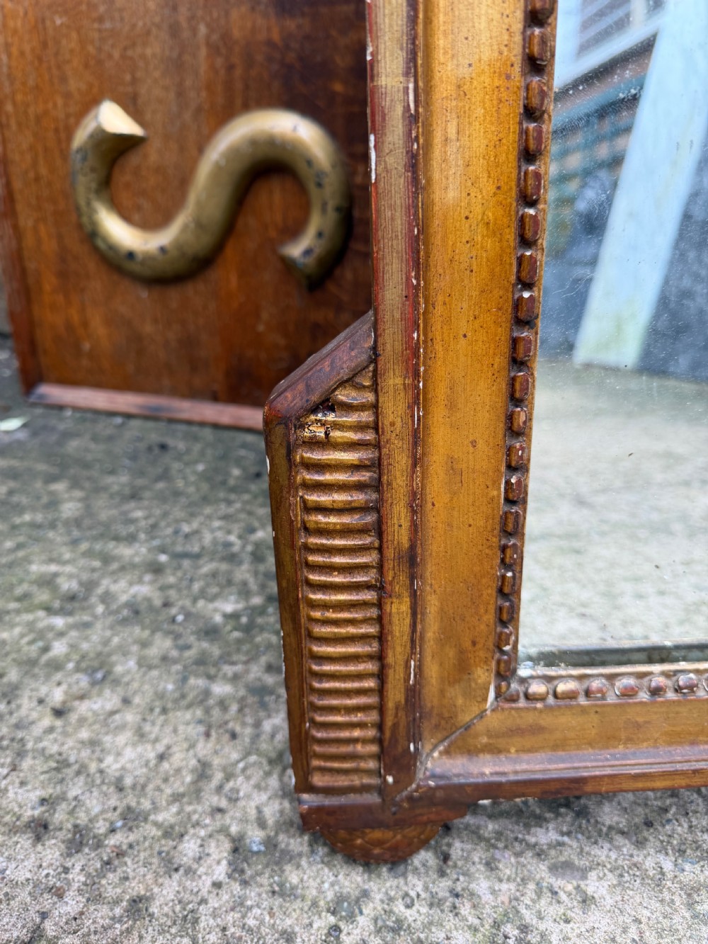 A large late eighteenth-century French giltwood wall mirror featuring a carved fruit basket pediment, floral foliage, and a rectangular beaded frame. View V