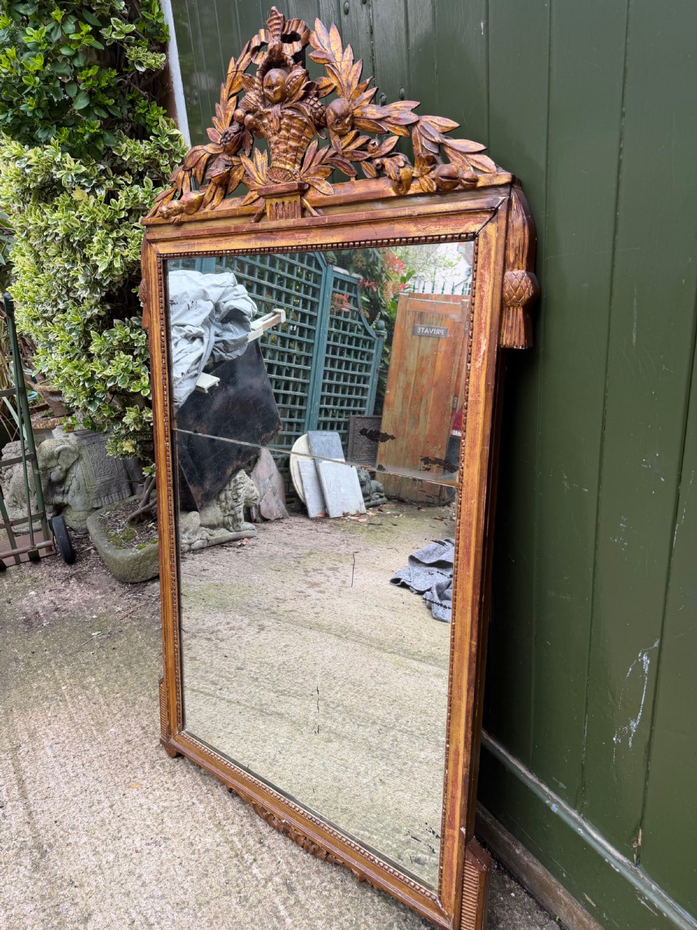 A large late eighteenth-century French giltwood wall mirror featuring a carved fruit basket pediment, floral foliage, and a rectangular beaded frame. View VI