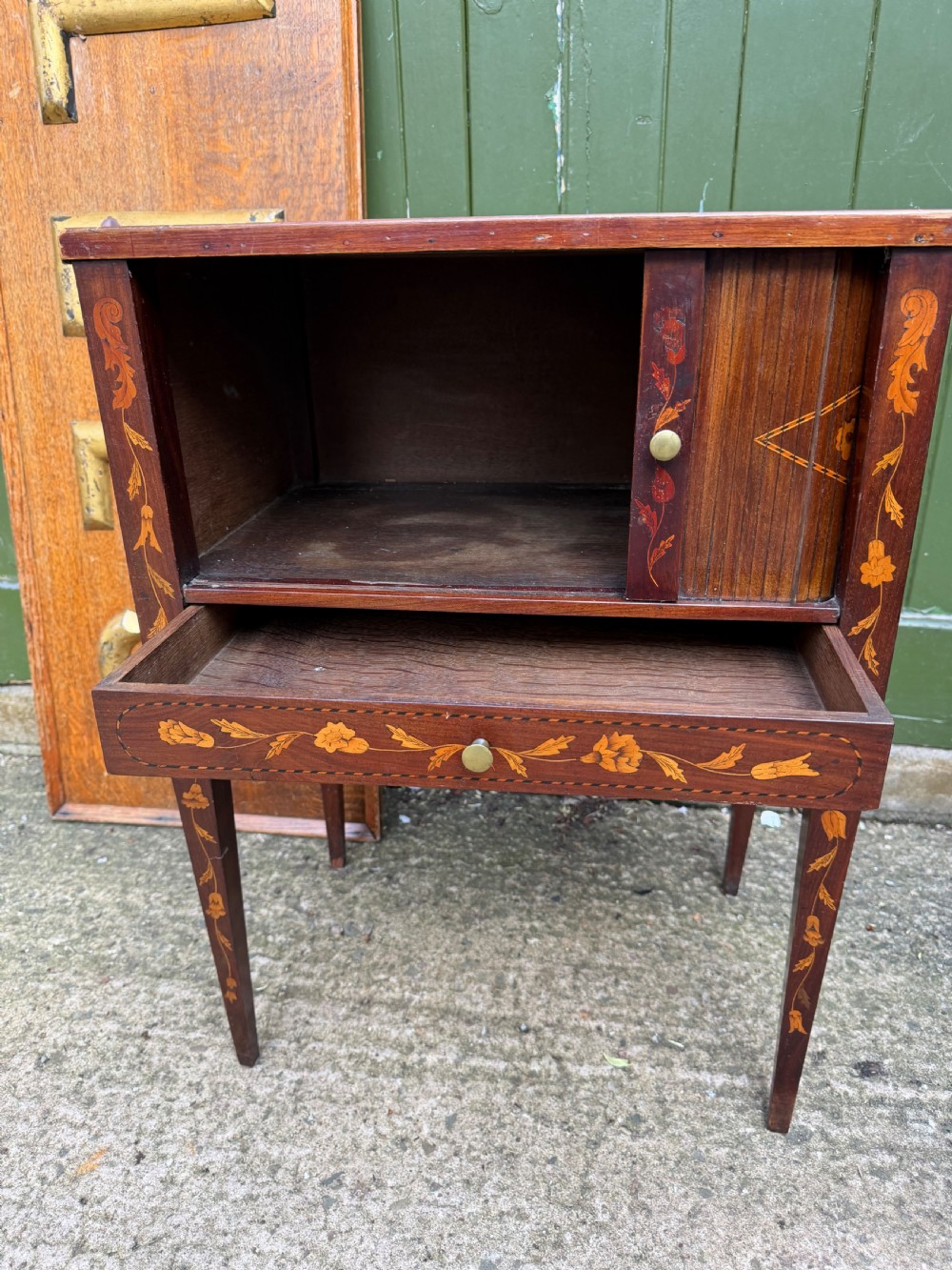 A Dutch mahogany bedside cupboard featuring floral marquetry inlays, a tambour slatted door, a single lower drawer with brass handles, and square tapered legs. View V