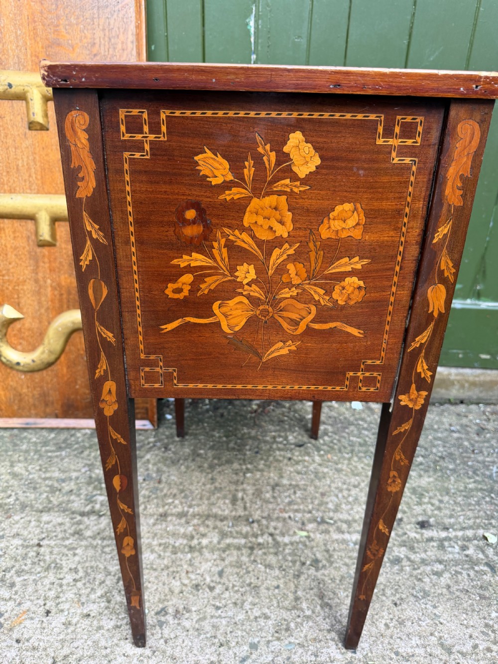 A Dutch mahogany bedside cupboard featuring floral marquetry inlays, a tambour slatted door, a single lower drawer with brass handles, and square tapered legs. View VI