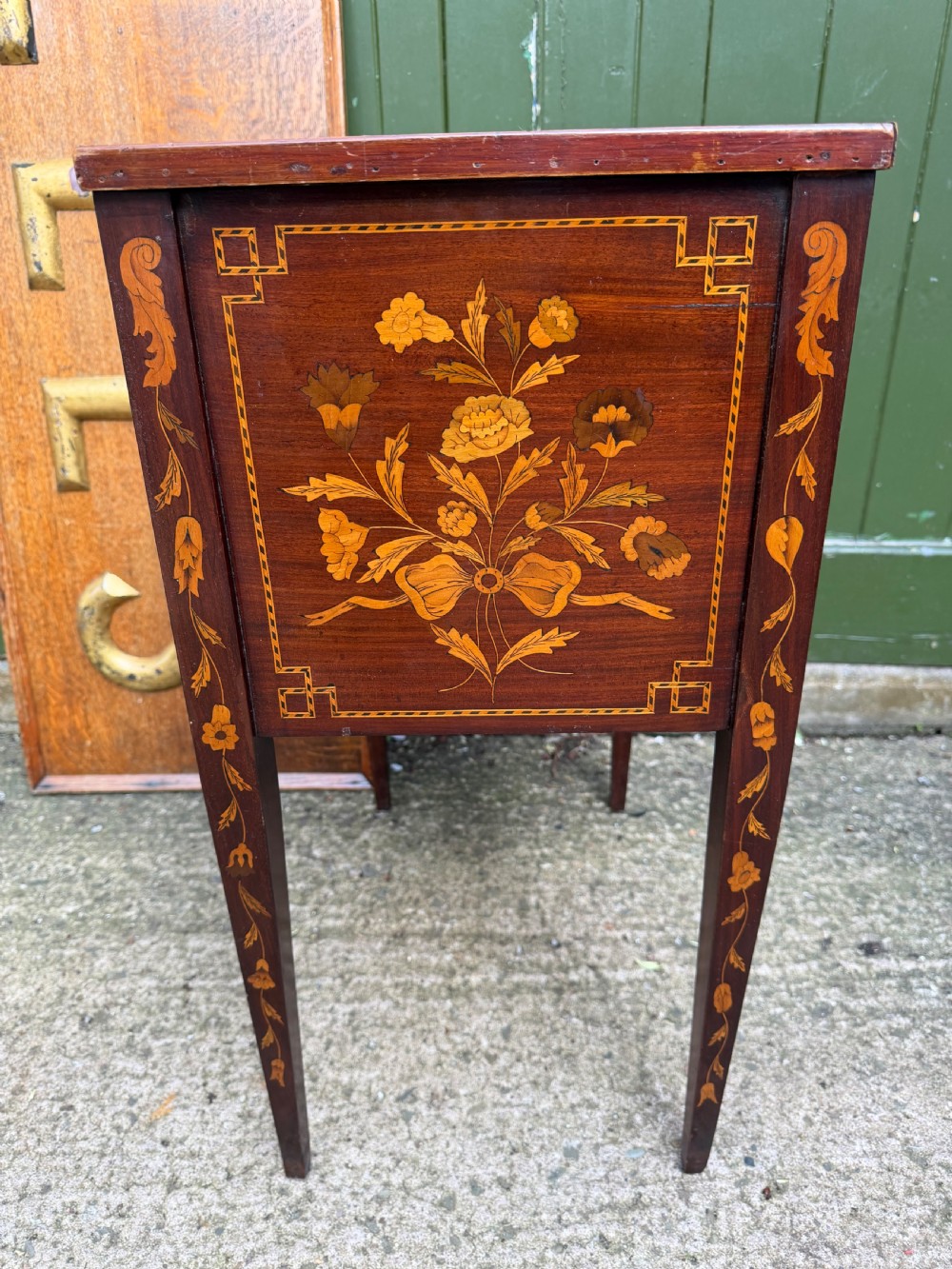 A Dutch mahogany bedside cupboard featuring floral marquetry inlays, a tambour slatted door, a single lower drawer with brass handles, and square tapered legs. View IX