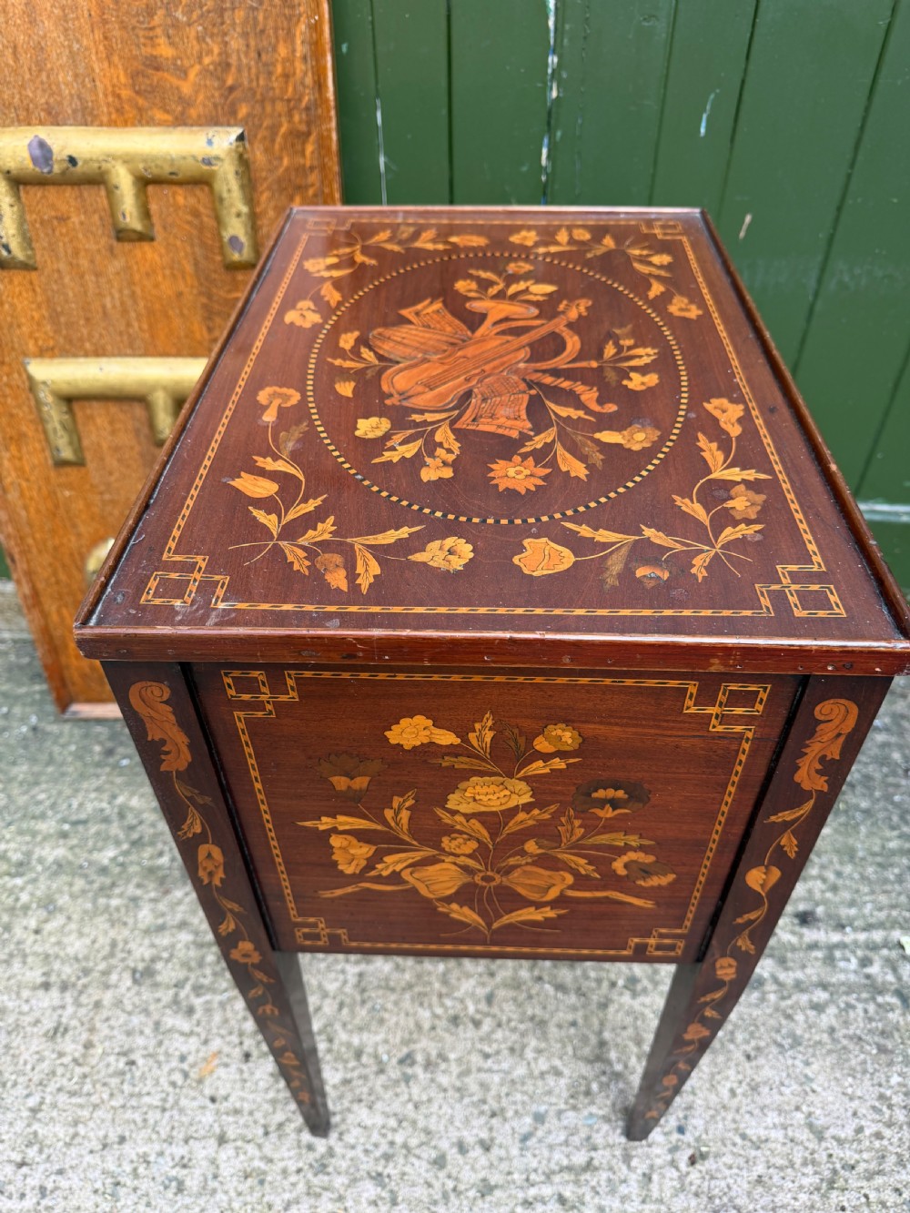 A Dutch mahogany bedside cupboard featuring floral marquetry inlays, a tambour slatted door, a single lower drawer with brass handles, and square tapered legs. View X
