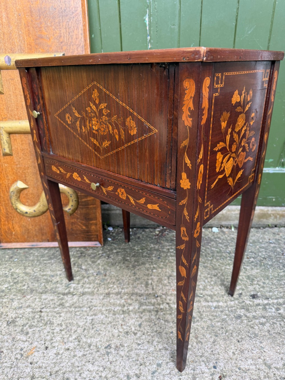 A Dutch mahogany bedside cupboard featuring floral marquetry inlays, a tambour slatted door, a single lower drawer with brass handles, and square tapered legs. View XI