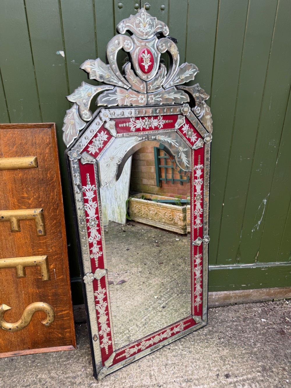 An antique Venetian wall mirror featuring cut and etched glass borders with ruby red glass accents and a decorative pediment crest.