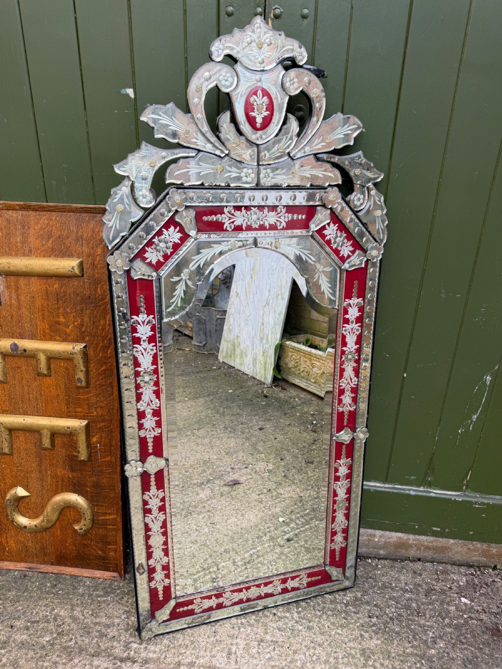 An antique Venetian wall mirror featuring cut and etched glass borders with ruby red glass accents and a decorative pediment crest. View VI