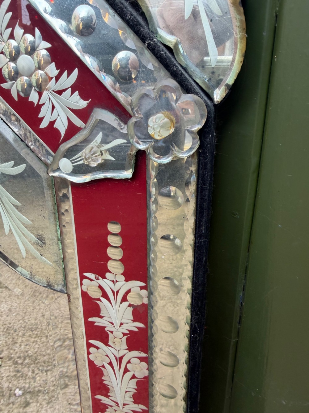 An antique Venetian wall mirror featuring cut and etched glass borders with ruby red glass accents and a decorative pediment crest. View X