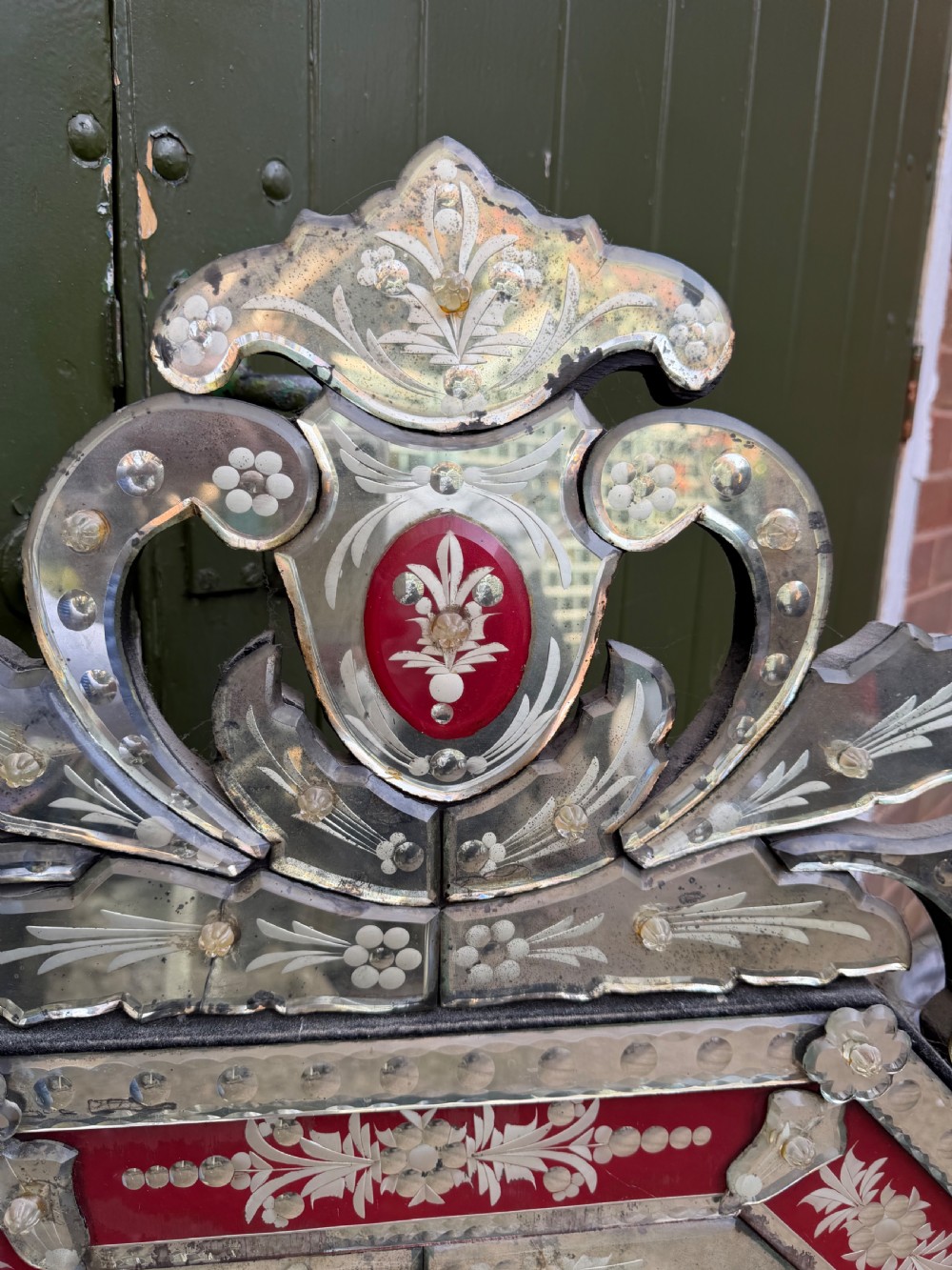 An antique Venetian wall mirror featuring cut and etched glass borders with ruby red glass accents and a decorative pediment crest. View XIX