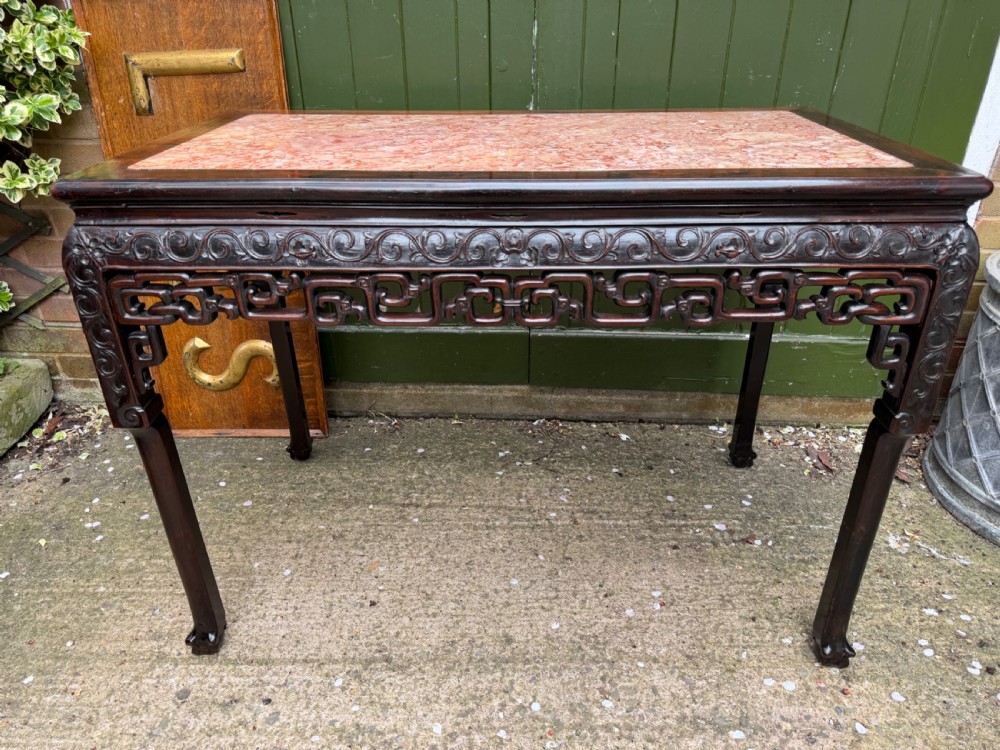 Late 19th-century Chinese Qing Dynasty dark hardwood centre table featuring an inset pink rouge marble rectangular top and intricately carved fretwork aprons.