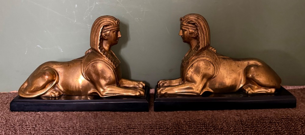 A pair of early nineteenth-century gilded bronze recumbent sphinxes resting on rectangular dark patinated bronze plinth bases.