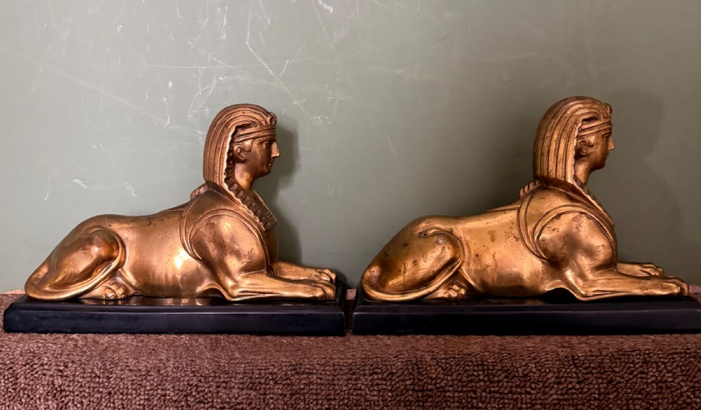 A pair of early nineteenth-century gilded bronze recumbent sphinxes resting on rectangular dark patinated bronze plinth bases. View II