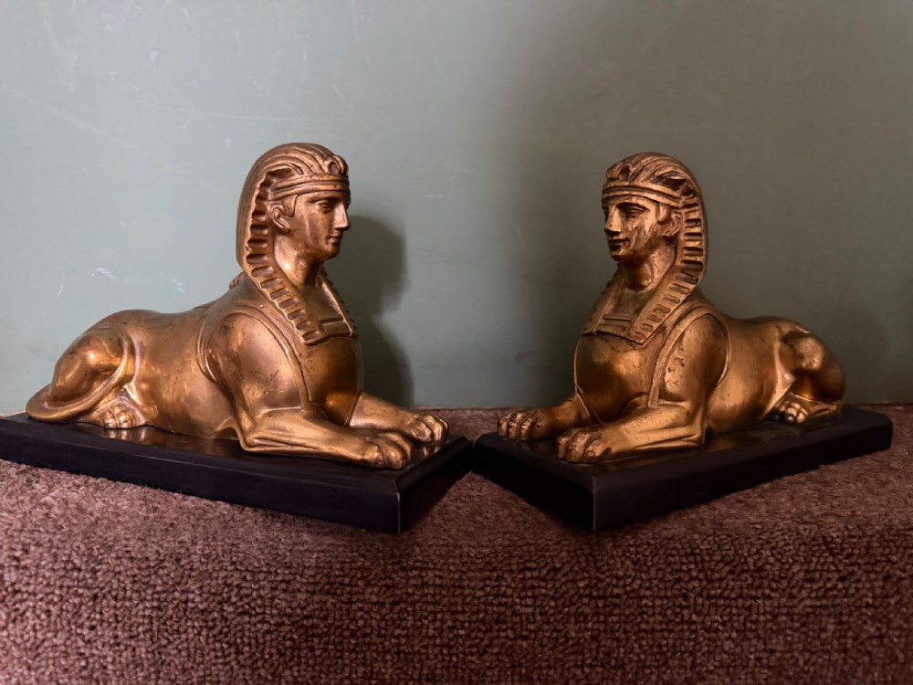 A pair of early nineteenth-century gilded bronze recumbent sphinxes resting on rectangular dark patinated bronze plinth bases. View XVI