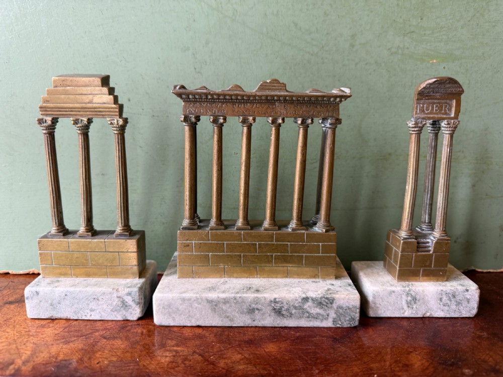 A set of three late 19th-century miniature polished bronze models representing ancient Roman temple ruins mounted on green marble bases.