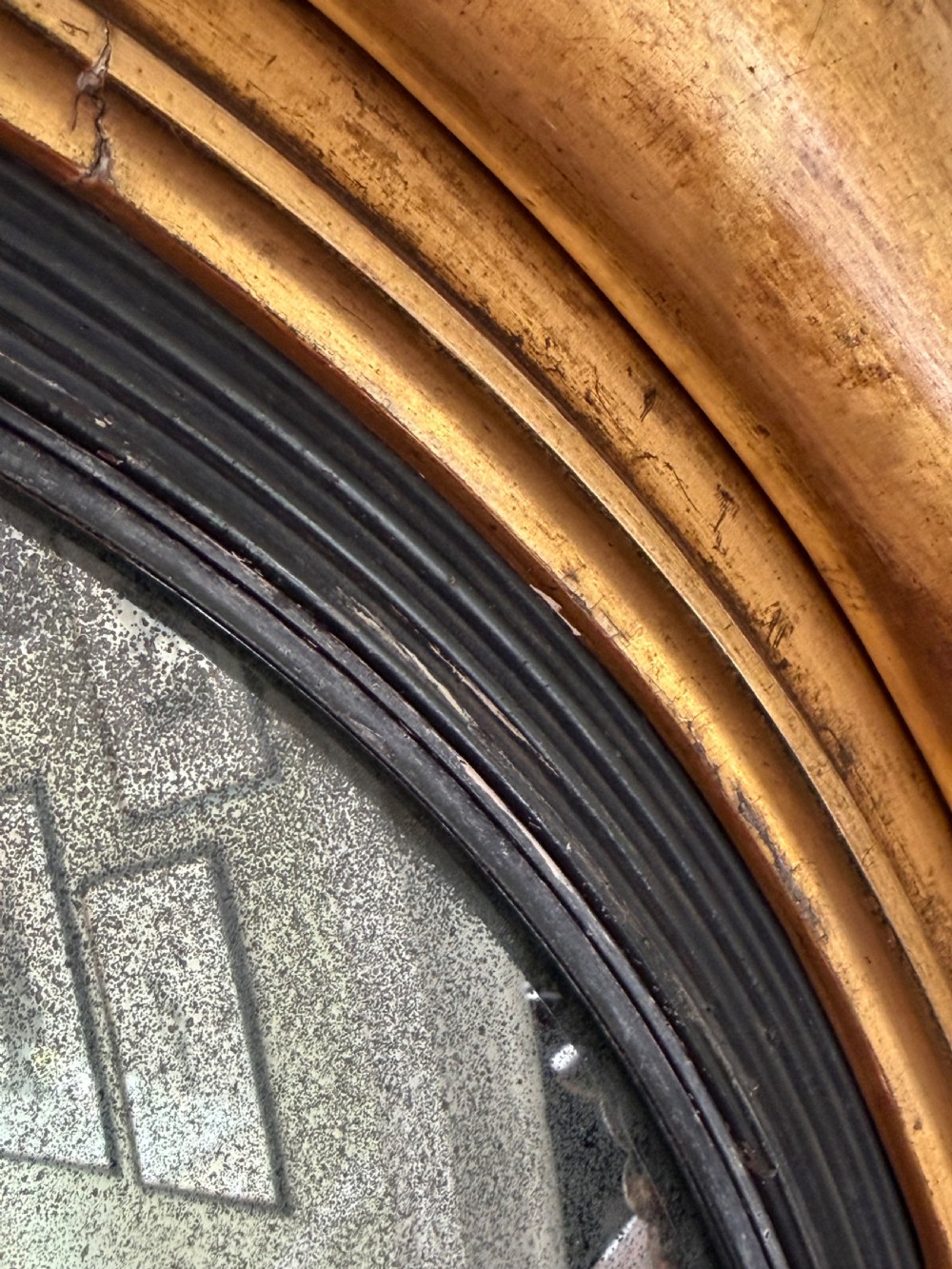 An early 19th-century Regency circular giltwood convex wall mirror featuring carved shell motifs, an ebonised reeded inner slip, and foxed mirror glass. View IX