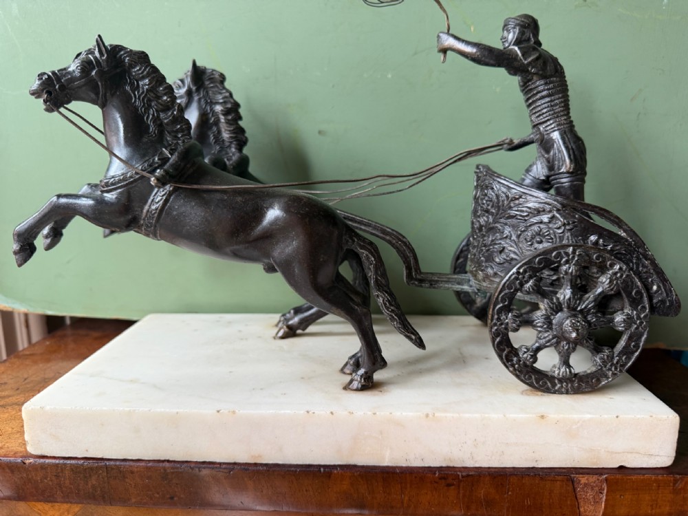 A mid-19th-century dark bronze sculpture depicting a Roman charioteer driving two rearing horses, mounted on a rectangular white marble plinth. View VIII