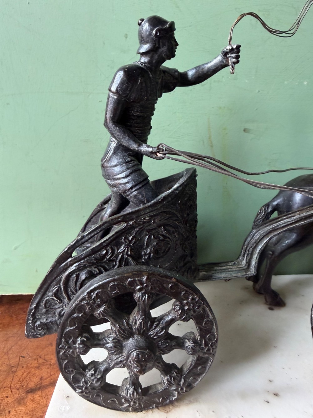 A mid-19th-century dark bronze sculpture depicting a Roman charioteer driving two rearing horses, mounted on a rectangular white marble plinth. View XII