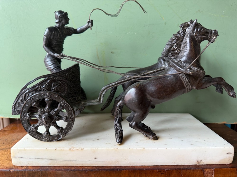 A mid-19th-century dark bronze sculpture depicting a Roman charioteer driving two rearing horses, mounted on a rectangular white marble plinth. View XXIII