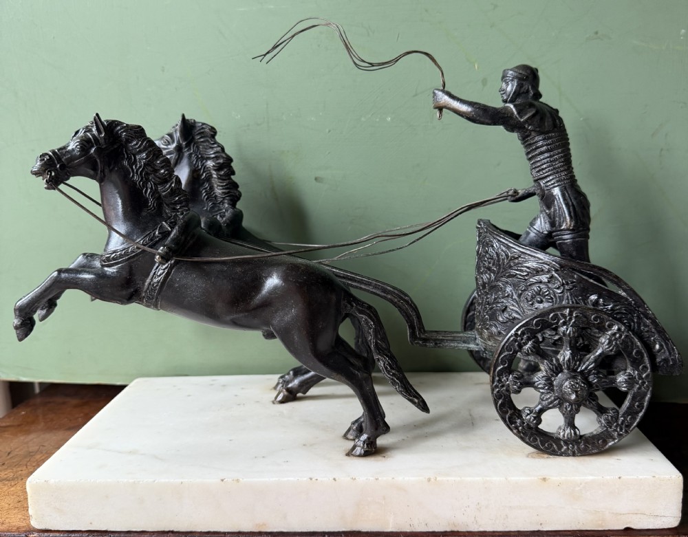 A mid-19th-century dark bronze sculpture depicting a Roman charioteer driving two rearing horses, mounted on a rectangular white marble plinth.