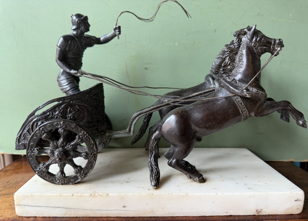 A mid-19th-century dark bronze sculpture depicting a Roman charioteer driving two rearing horses, mounted on a rectangular white marble plinth. View II