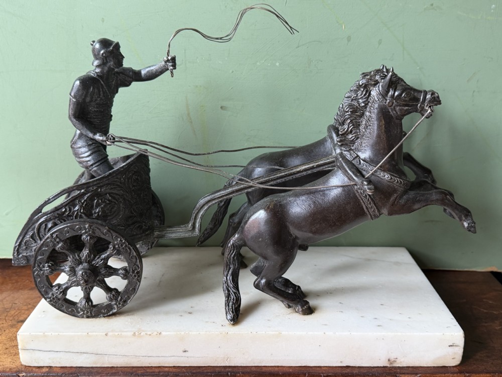 A mid-19th-century dark bronze sculpture depicting a Roman charioteer driving two rearing horses, mounted on a rectangular white marble plinth. View XI