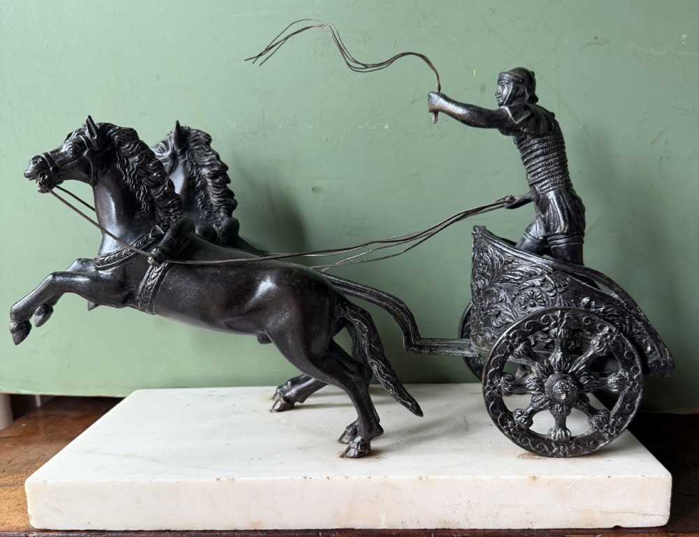 A mid-19th-century dark bronze sculpture depicting a Roman charioteer driving two rearing horses, mounted on a rectangular white marble plinth. View XXVI