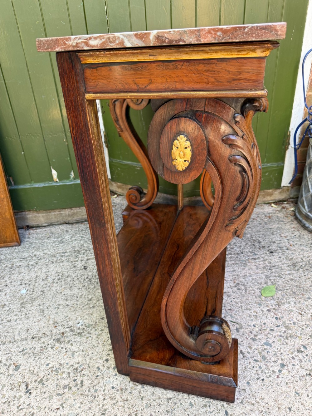 A Regency rosewood console table featuring a figured marble top, carved scroll legs with parcel-gilt details, an inset mirror back, and a plinth base. View VI