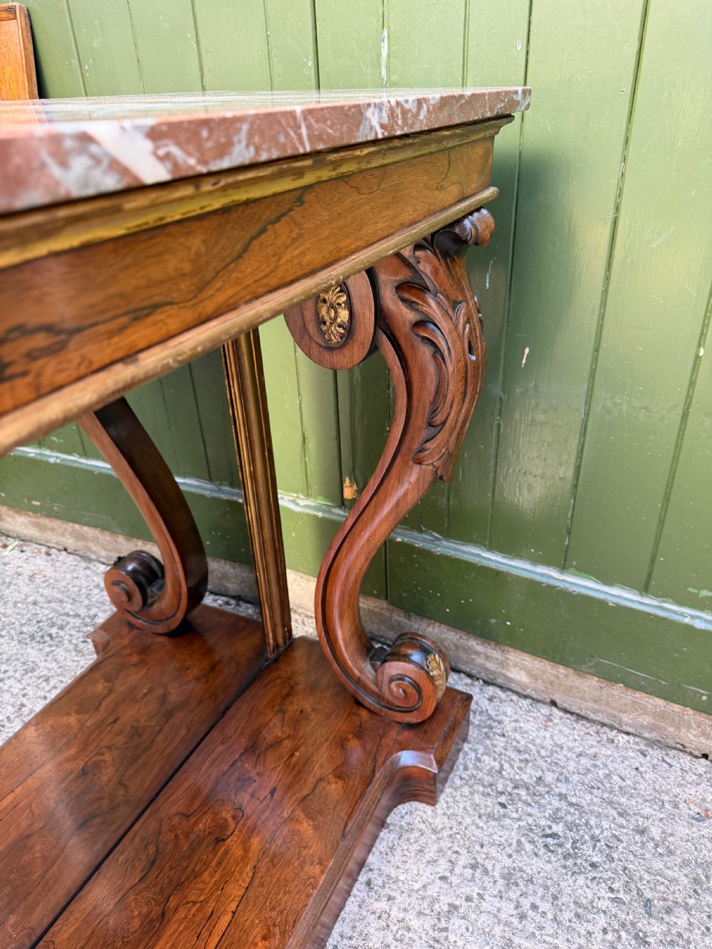 A Regency rosewood console table featuring a figured marble top, carved scroll legs with parcel-gilt details, an inset mirror back, and a plinth base. View X
