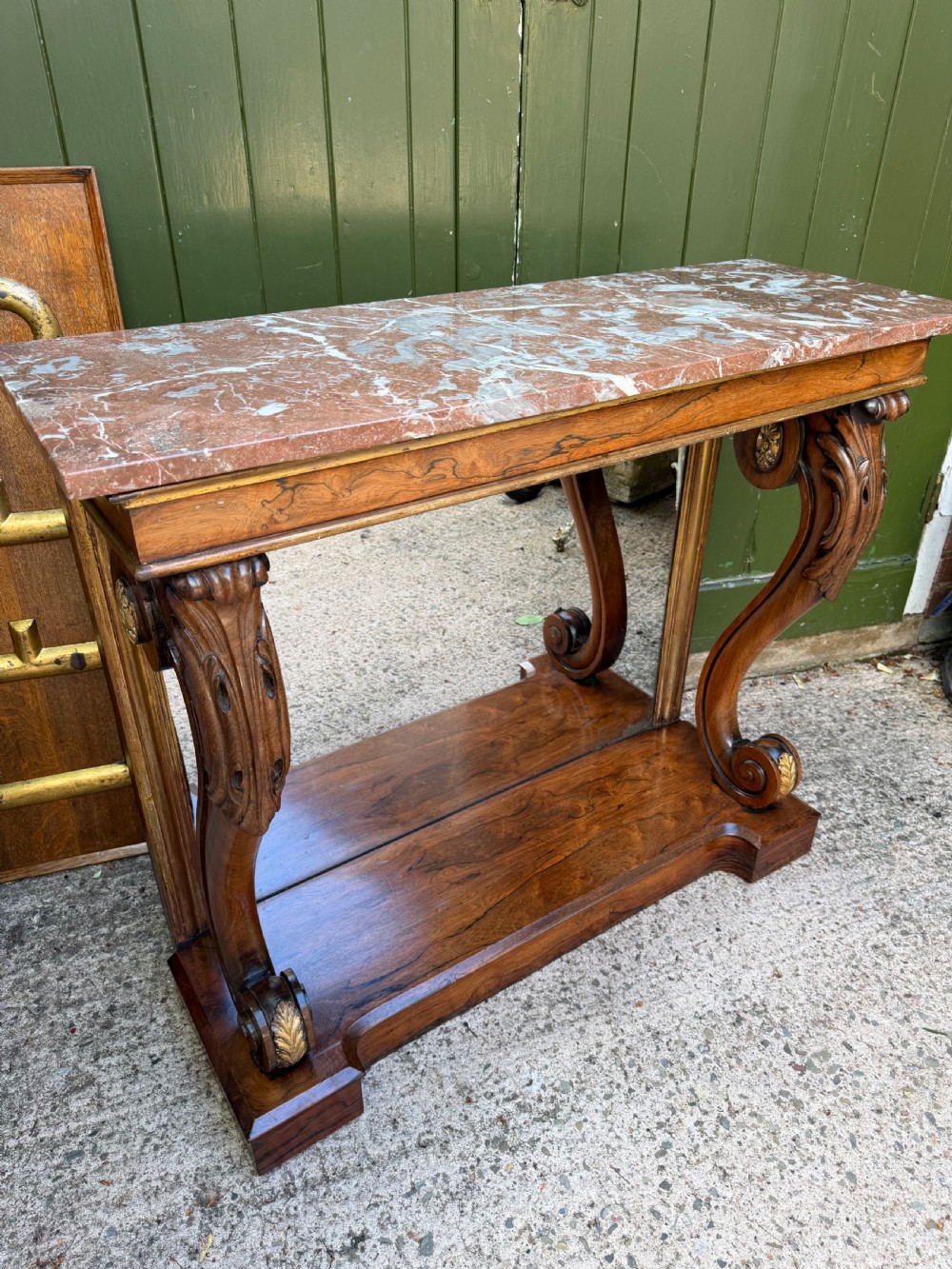 A Regency rosewood console table featuring a figured marble top, carved scroll legs with parcel-gilt details, an inset mirror back, and a plinth base. View XII