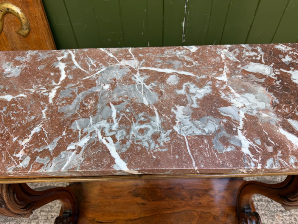 A Regency rosewood console table featuring a figured marble top, carved scroll legs with parcel-gilt details, an inset mirror back, and a plinth base. View XV