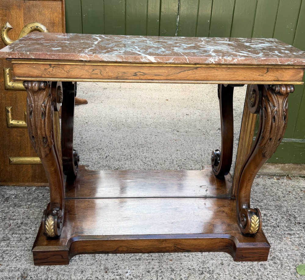 A Regency rosewood console table featuring a figured marble top, carved scroll legs with parcel-gilt details, an inset mirror back, and a plinth base. View XIII