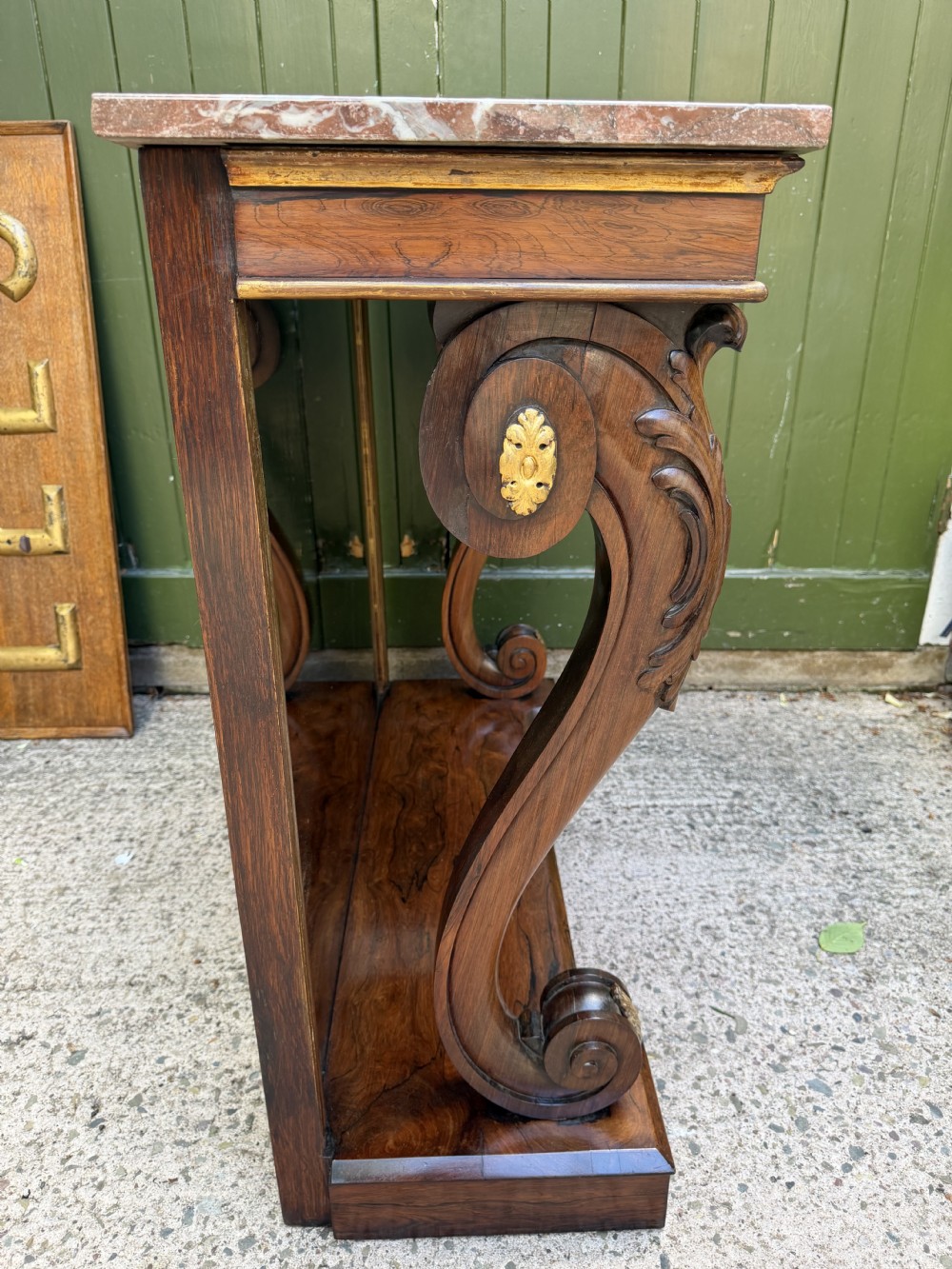 A Regency rosewood console table featuring a figured marble top, carved scroll legs with parcel-gilt details, an inset mirror back, and a plinth base. View XX